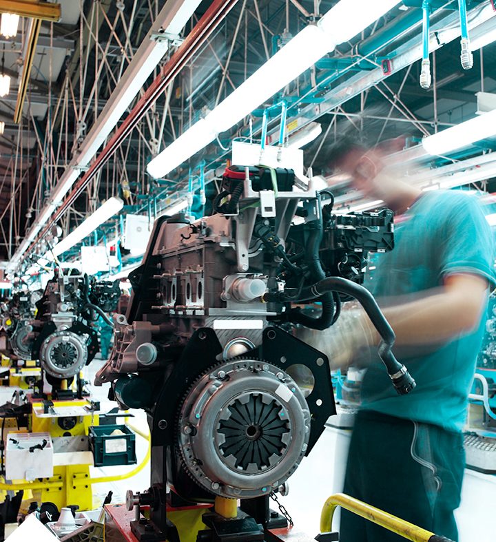 Mitarbeiter montiert Motoren in einer Fabrikhalle mit Maschinen und Werkzeugen.