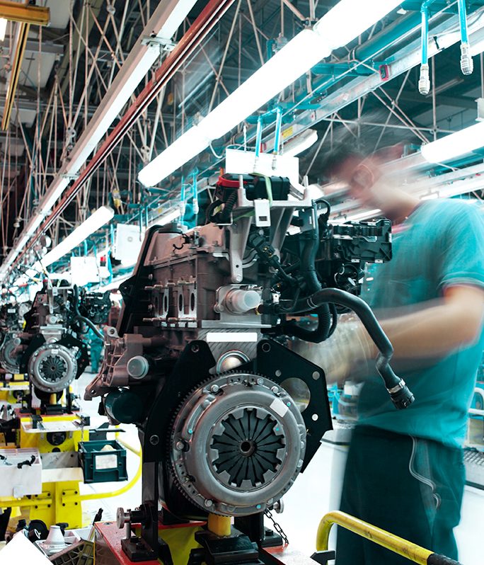 Arbeiter montiert Motoren in einer Fabrikhalle mit leuchtenden Deckenlichtern.