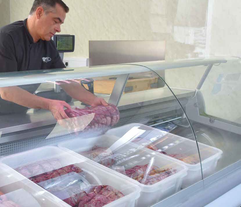 Fleischer legt Fleisch in einem Verkaufstresen mit verschiedenen Behältern mit Fleischsorten.